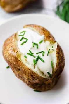 a baked potato with sour cream and green sprinkles on a white plate