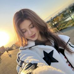 a girl is standing on the street and looking at her cell phone while wearing a star jacket