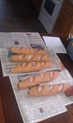 a person is pointing at some breads on a newspaper while another person sits in the background