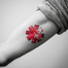 a red and white medical symbol tattoo on the left inner arm with watercolor paint splatters