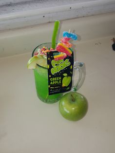 a green apple sitting next to a drink in a cup on top of a counter