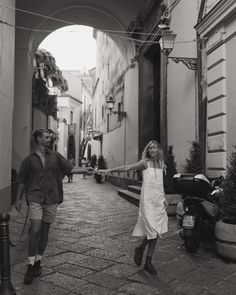 a man and woman walking down an alleyway holding their arms out to each other