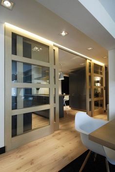 an open glass door leading to a dining room with wooden floors and white chairs in front of it