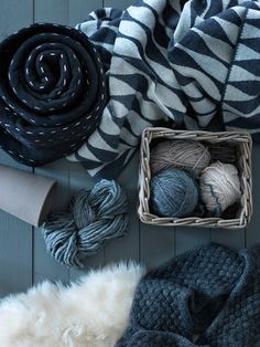 several balls of yarn are sitting on the floor next to a basket with two skeins