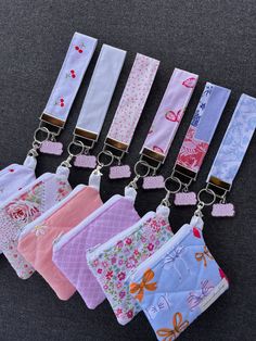 six small purses with key chains attached to them are lined up on a gray surface