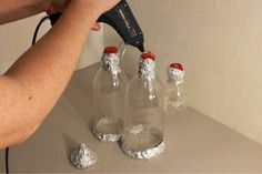 a woman is using an electric hair dryer on four empty soda bottles with silver foil wrapped around them