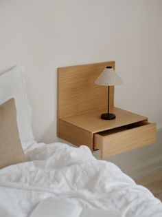 a bed with white sheets and a wooden night stand on top of it next to a lamp