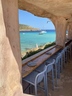 there are many chairs that are sitting at the long table by the water's edge