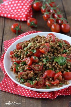 a white bowl filled with lentils and tomatoes on top of a red polka dot napkin