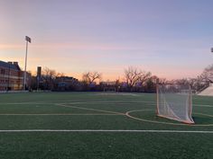 an empty soccer field at sunset with the goal in the foreground and buildings in the background