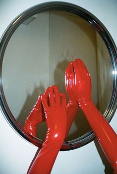 two hands in red latex gloves are reflected in a round mirror on the wall