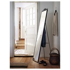 a large mirror sitting on top of a wooden floor next to a basket and coat rack