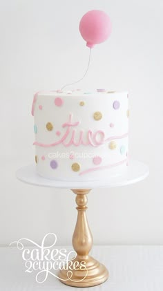 a white cake with pink and gold polka dots on it, topped with a balloon