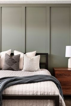 a bed with pillows and blankets on top of it next to a night stand in front of a green wall