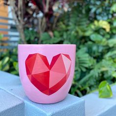 a pink cup with a red heart on it sitting on top of a cement block