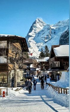 people are walking in the snow near some buildings and mountain range with snow on it