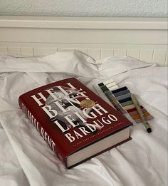 two books are sitting on top of a bed with white sheets and pillows, next to each other