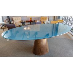 an oval glass table with wooden base in a room filled with chairs and couches