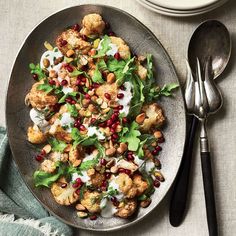 a plate filled with cauliflower, nuts and greens next to silverware on a table