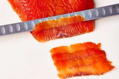 two pieces of fish sitting on top of a white plate next to a large knife