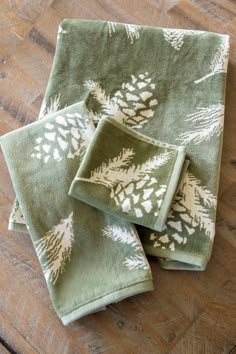 three green towels with white pine cones on them sitting on a wooden floor next to a pair of scissors