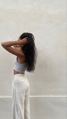 a woman standing in front of a white wall with her hands on her head and arms behind her head