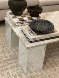 a white marble coffee table with two vases on top and books stacked on it