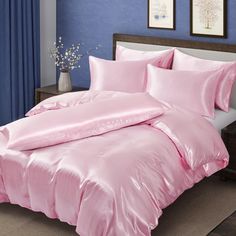 a bed with pink sheets and pillows in a blue room next to a vase filled with flowers