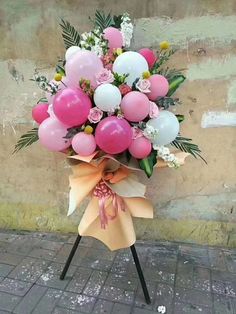 a bunch of balloons are tied to a pole on the sidewalk with pink and white flowers