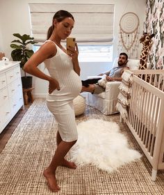 a woman standing in front of a baby crib taking a photo with her phone