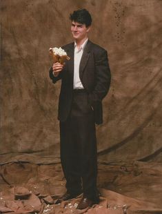 a young man in a suit and tie holding a piece of cake with icing on it