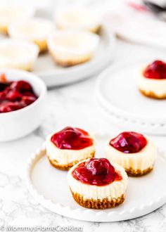 mini cheesecakes with raspberry sauce on white plates next to other desserts