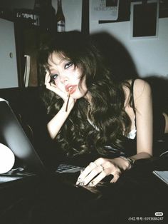 a woman laying on top of a black couch with her hand near her face while using a laptop computer