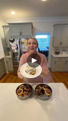 a woman holding a plate full of cupcakes on a kitchen counter with two other plates in front of her