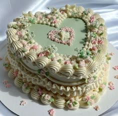 a heart shaped cake on a white plate with pink and green flowers around the edges