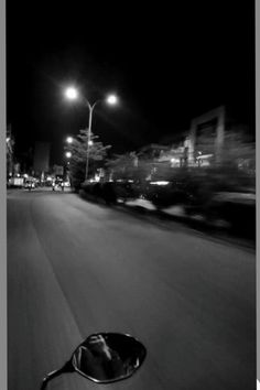 a black and white photo of a street at night with cars passing by in the distance