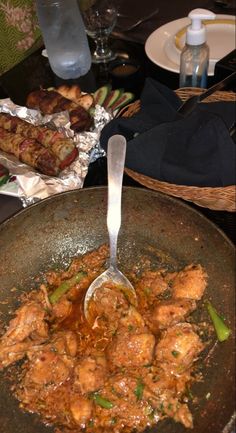 a skillet filled with meat and vegetables on top of a table next to plates