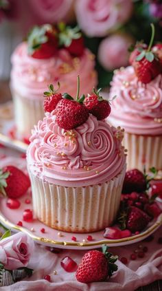 two cupcakes with pink frosting and strawberries on top are sitting next to each other