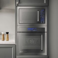 two stainless steel ovens in a kitchen with white counter tops and gray cabinets, one is built into the wall