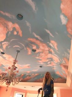 a woman is standing on a ladder in front of a painted ceiling with pink clouds