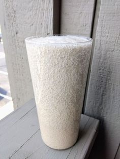 a tall white cup sitting on top of a wooden table next to a window sill