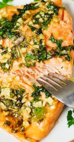 a white plate topped with salmon covered in sauce and greens next to a silver fork