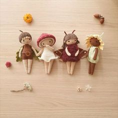 three little knitted dolls sitting next to each other on a wooden surface with flowers and leaves