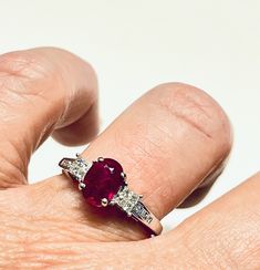 a woman's hand holding a ring with an oval shaped ruby and diamond set in the middle