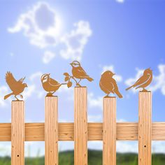 birds sitting on top of wooden posts in front of blue sky with clouds and sun