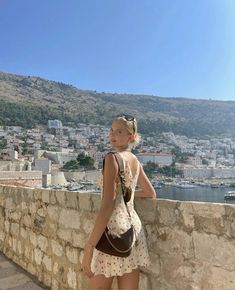 a woman standing on the side of a stone wall next to a body of water