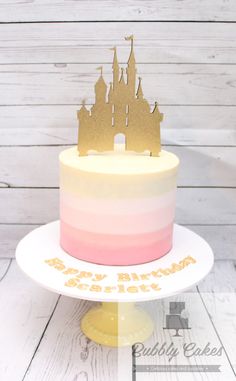 a birthday cake with a castle on top and gold foil lettering that says happy birthday