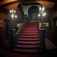 a red carpeted staircase leading up to a doorway with two chandeliers on either side