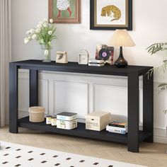 a black console table with books and pictures on the wall above it in a living room