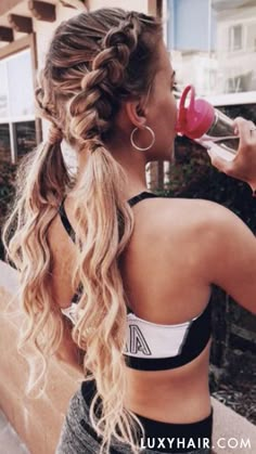 a woman with long hair drinking from a water bottle while standing on the side walk